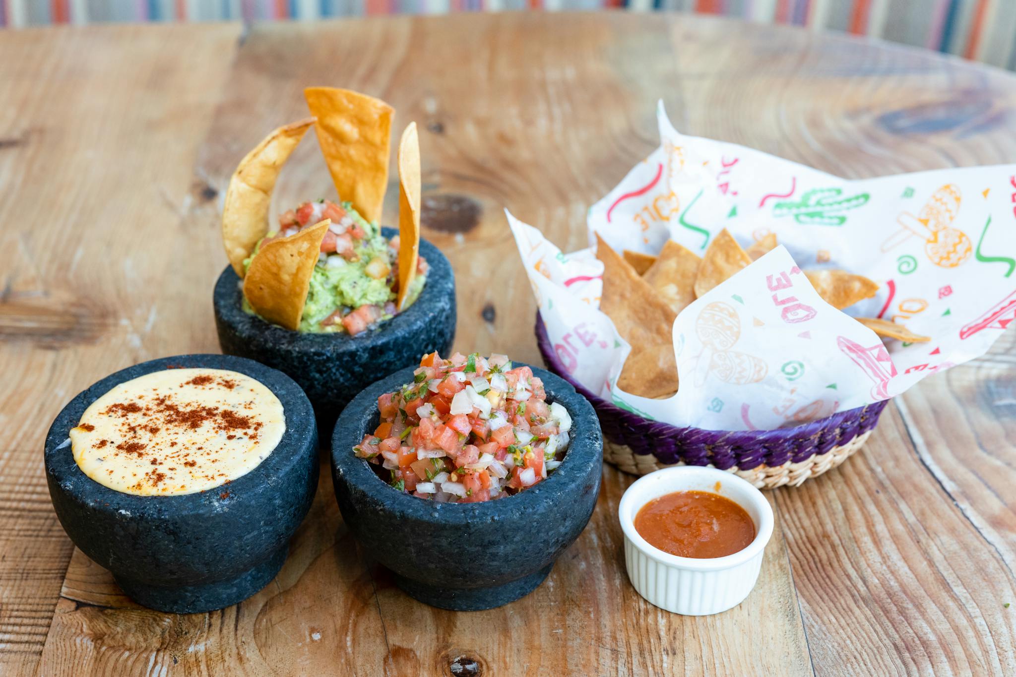 Delicious Mexican food spread featuring guacamole, salsa, and queso in molcajetes with tortilla chips.